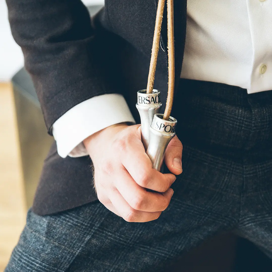 Hand grasping a pair of jump rope handles which are emblazoned with the logo of a popular Italian menswear designer.