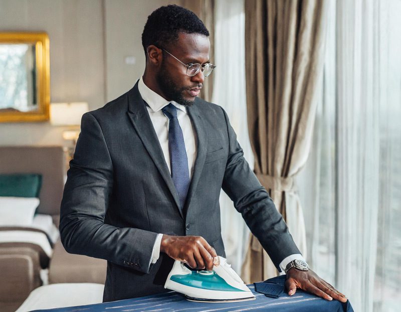 business man ironing a necktie to remove wrinkles, in a hotel room