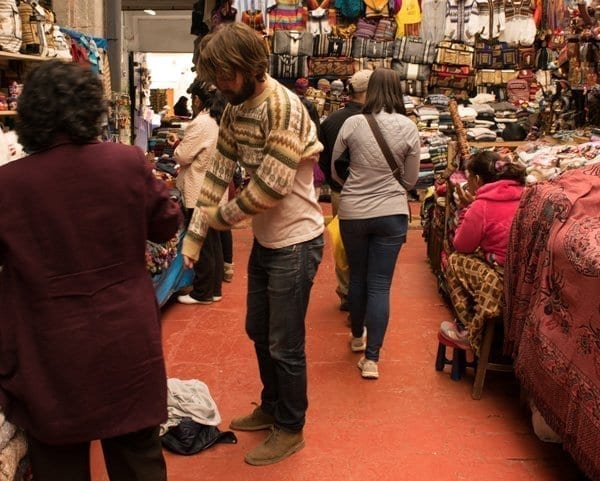 man tries on a sweater in outdoor market Peru